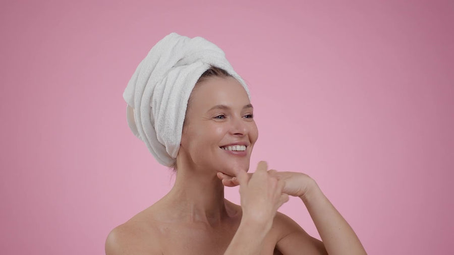 Smiling woman in a towel touching her glowing skin